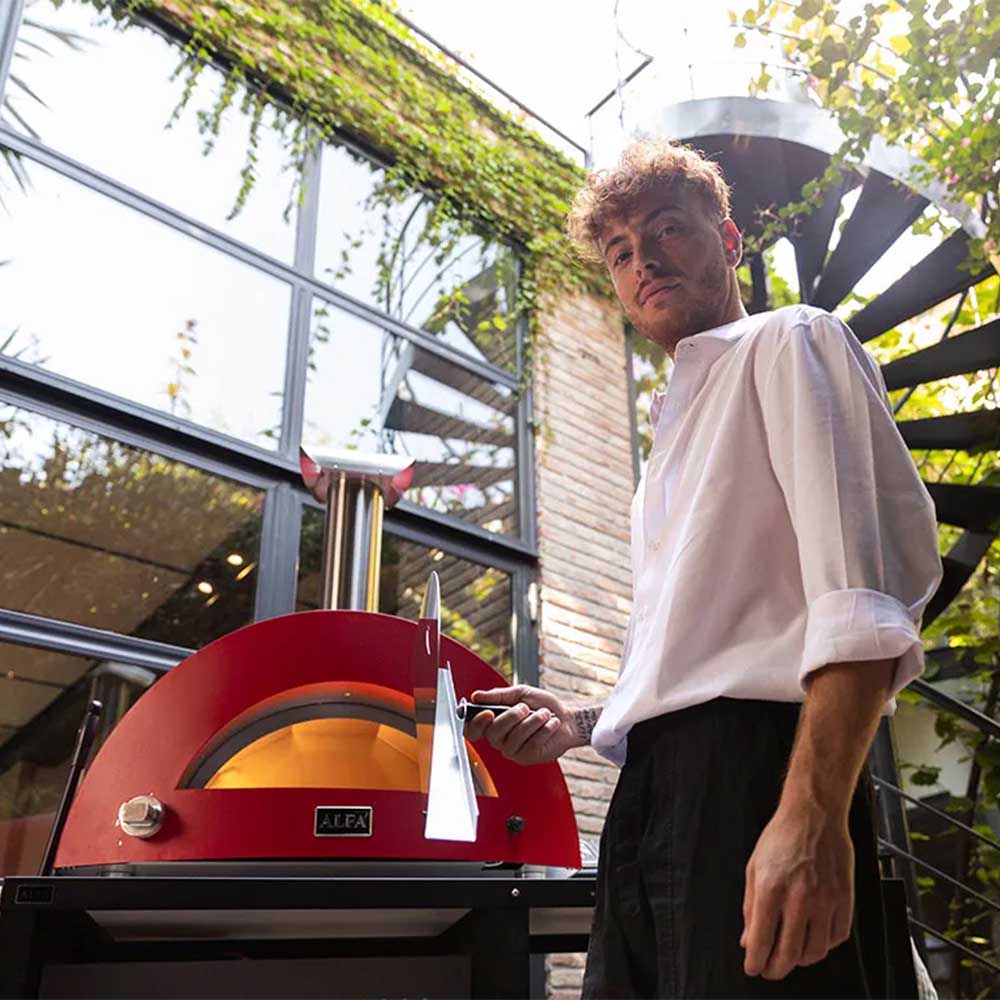 Wood-fired pizza oven with red dome as chef holds a pizza peel