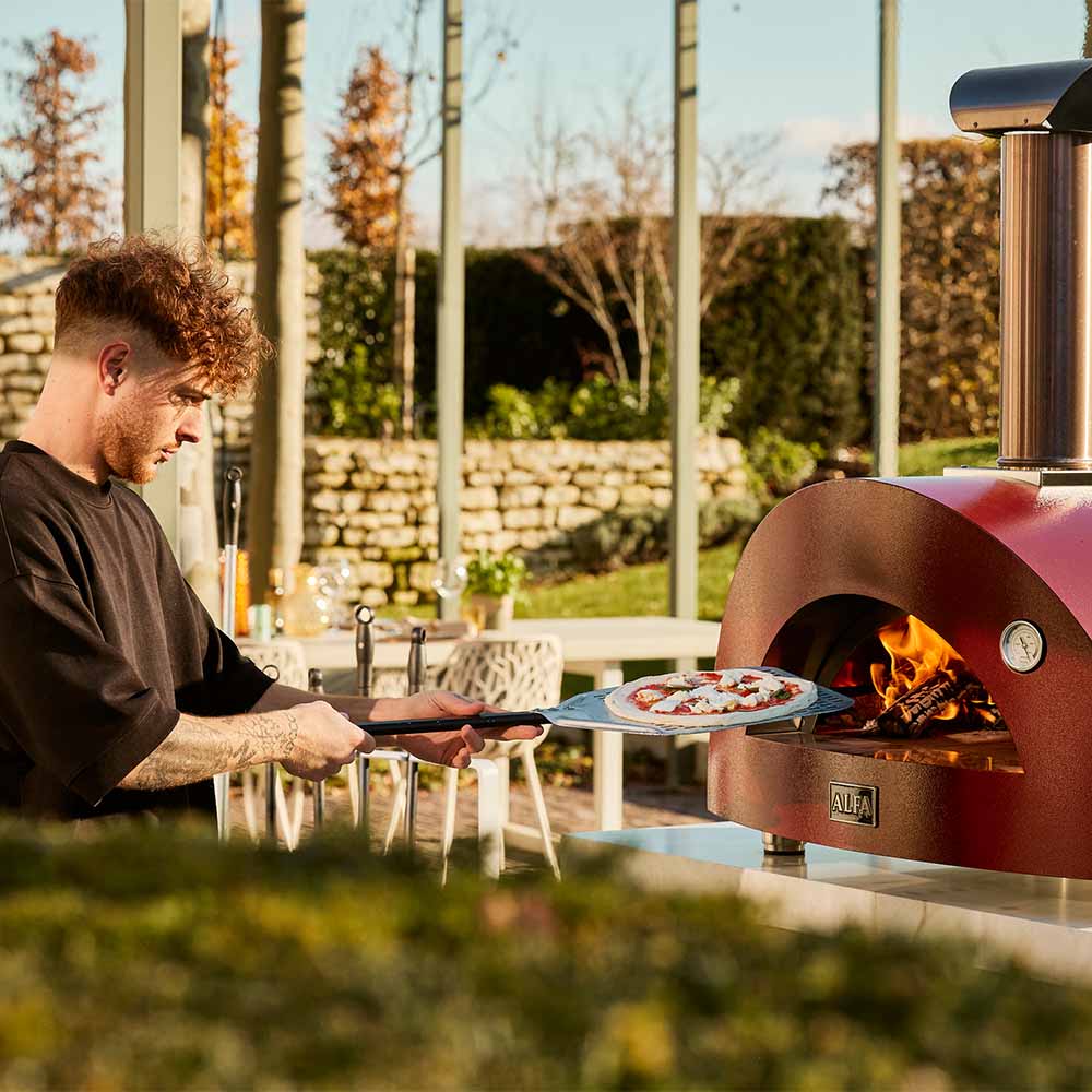Red wood-fired pizza oven with a chef holding a pizza on a metal peel