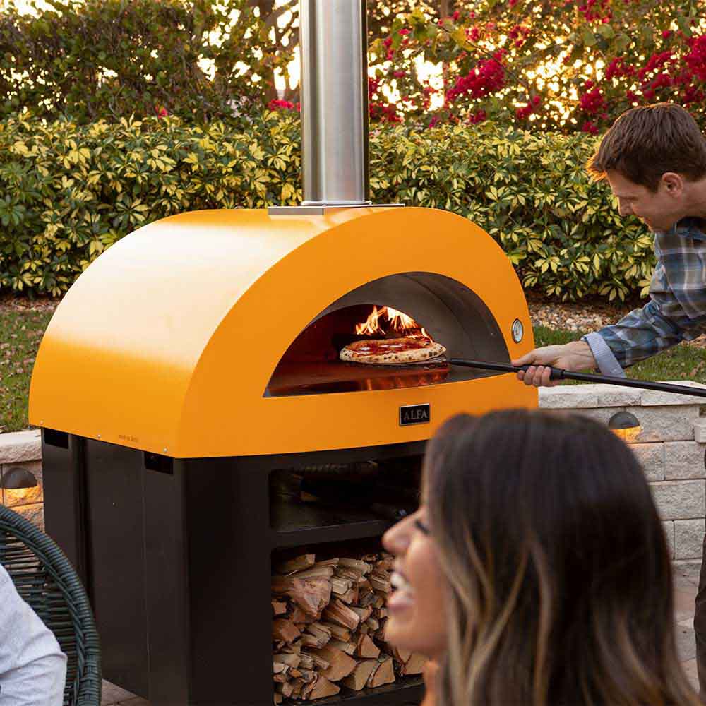 Freestanding gas pizza oven with yellow dome, flames inside, and a pizza on the stone