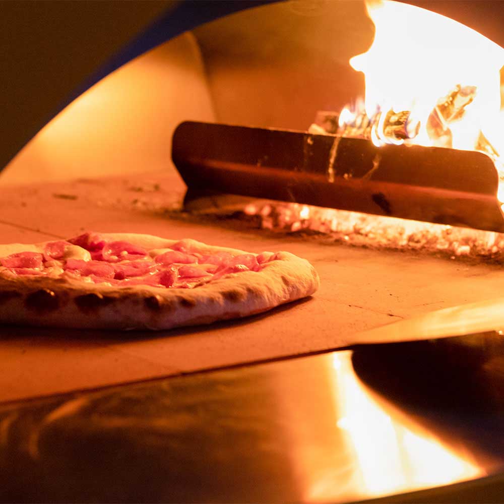 Oven baking stone with pizza on it; flames and oven interior surround the crust.