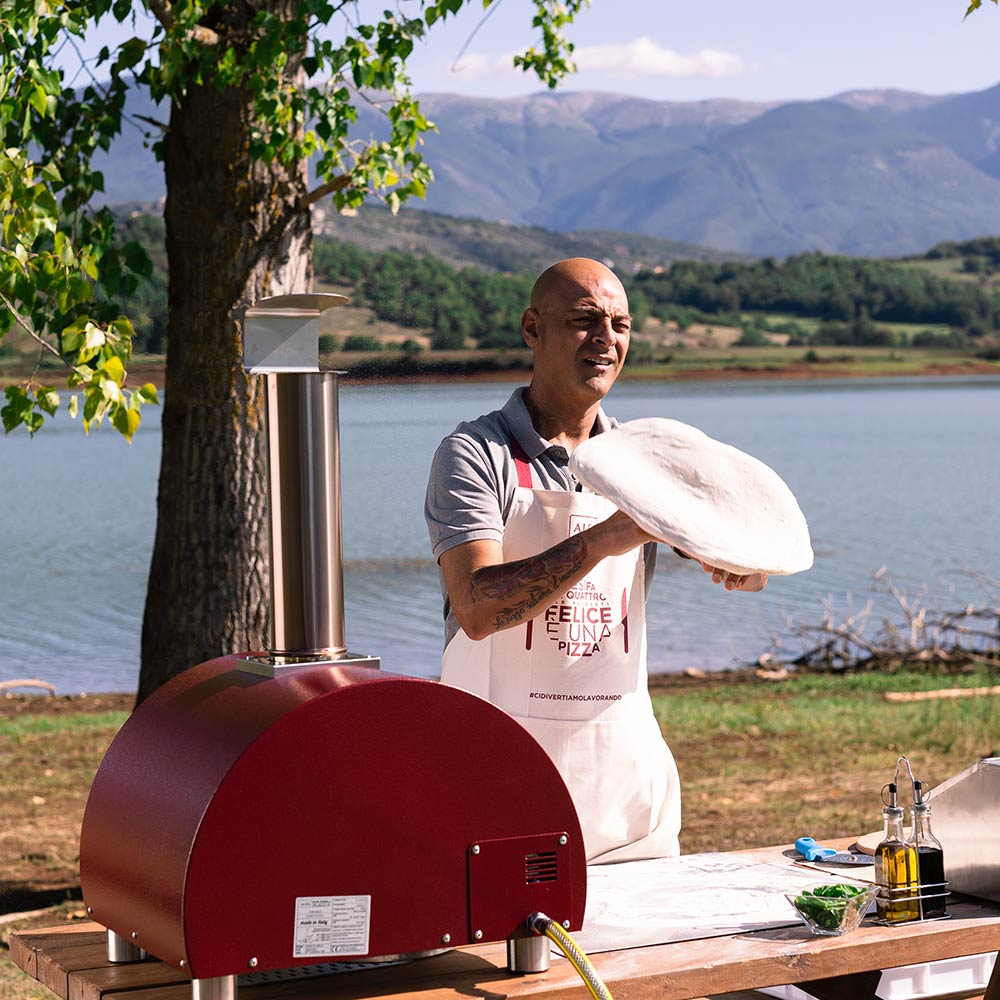 Portable gas pizza oven with red dome and tall chimney on outdoor countertop