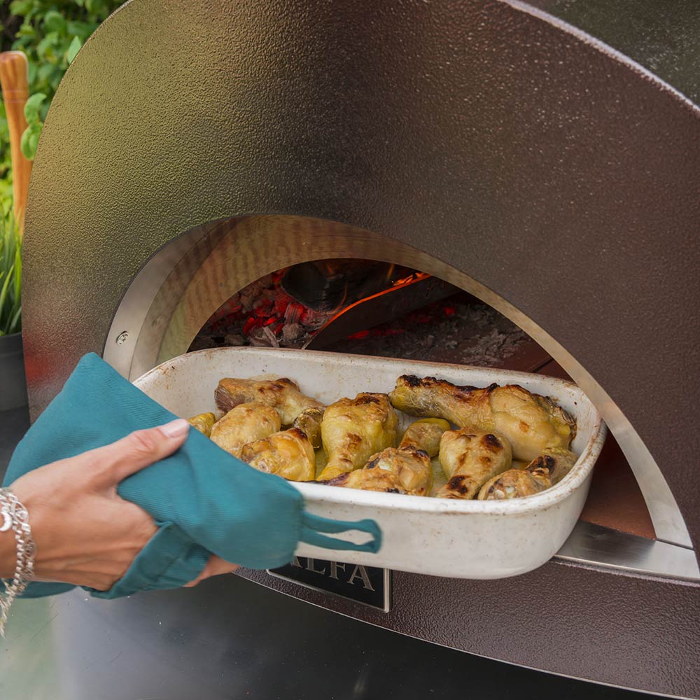 Wood-fired pizza oven with baking tray being placed into the firebox opening