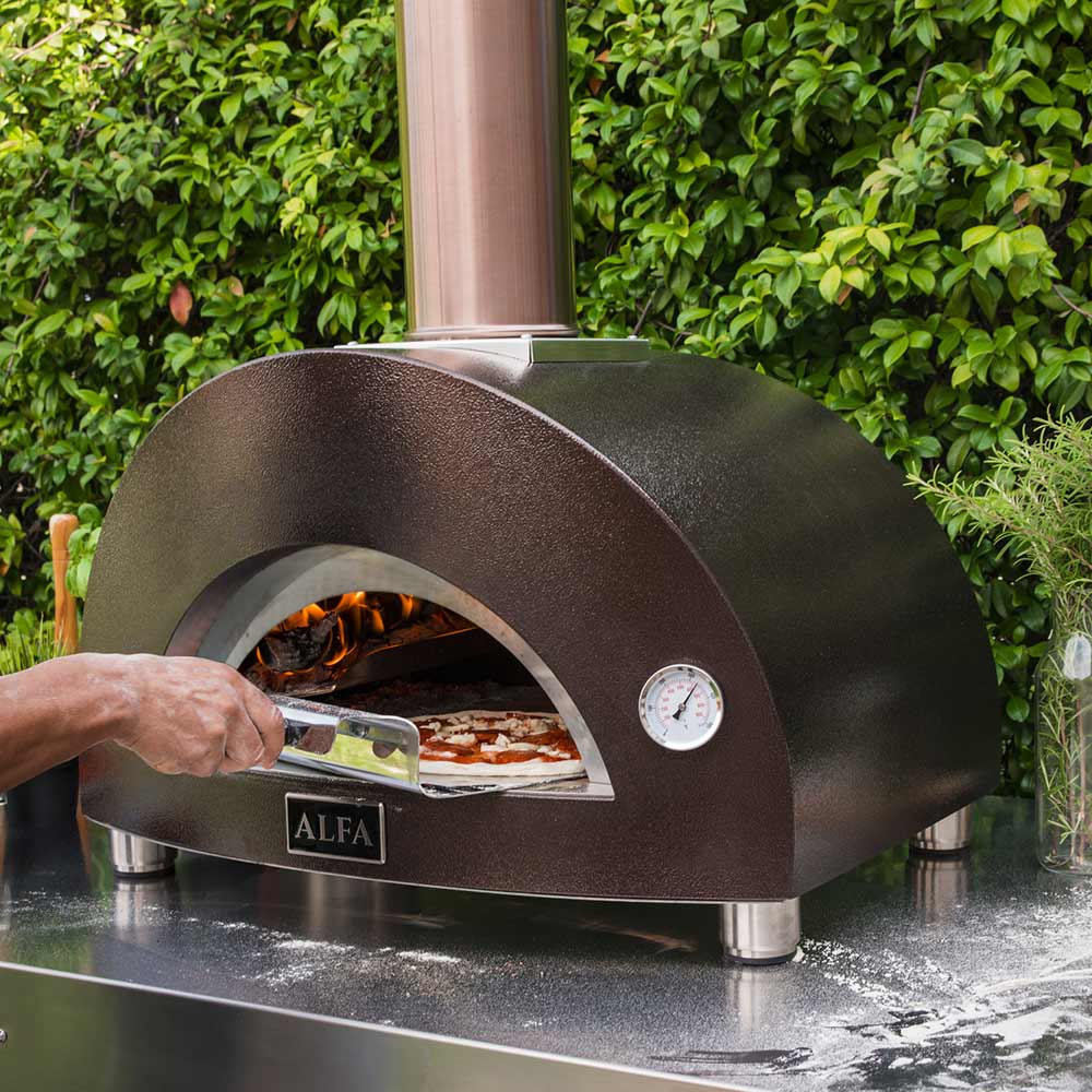 Wood-fired pizza oven with pizza being slid into the arched firebox, flame glow inside