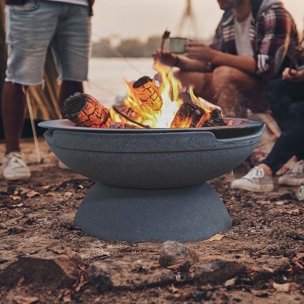 Portable fire pit with burning logs in dark gray bowl on outdoor ground