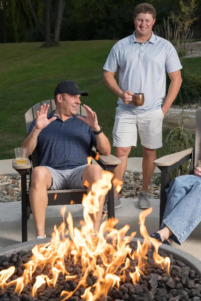 Two men laughing and discussing outdoor living near a backyard fire pit