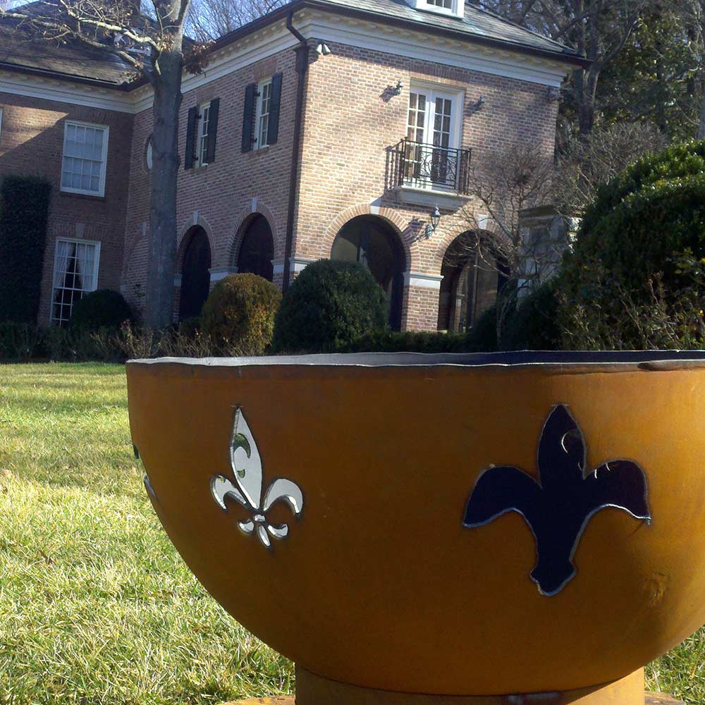 Rust-colored gas fire pit bowl with fleur de lis and butterfly metal cutouts