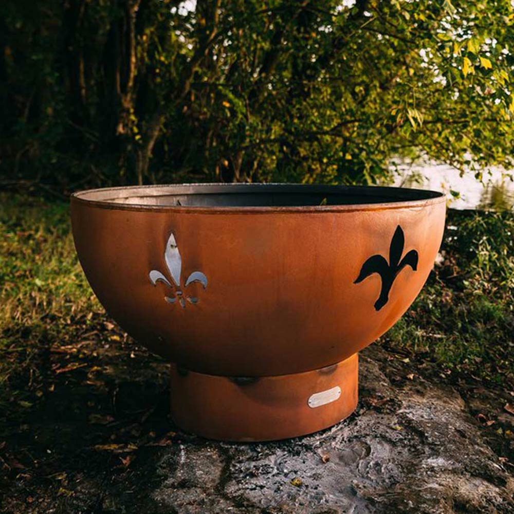 Rust-colored gas fire pit bowl with fleur de lis metal cutouts on the front