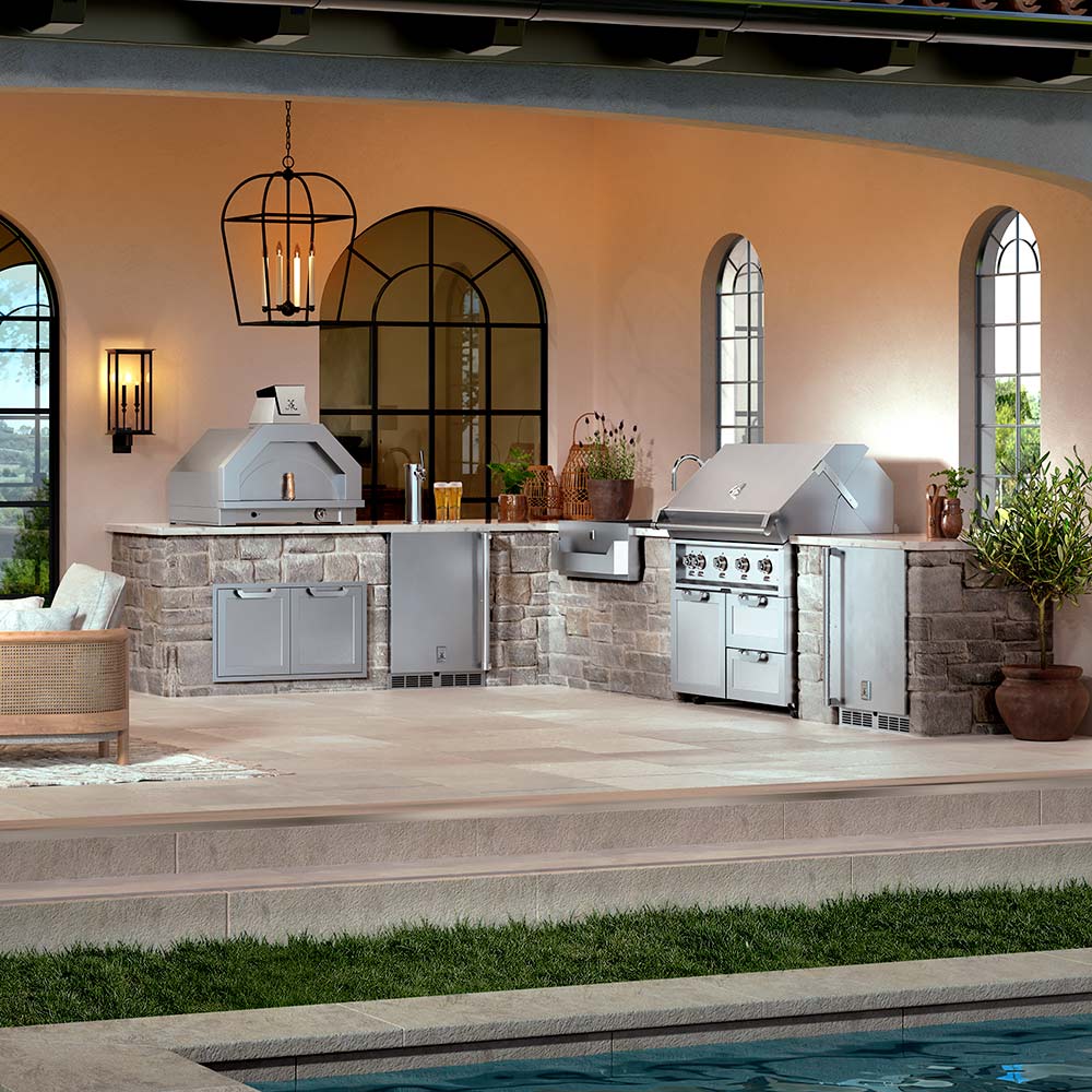 Outdoor kitchen with grills and appliances near a pool by Hestan