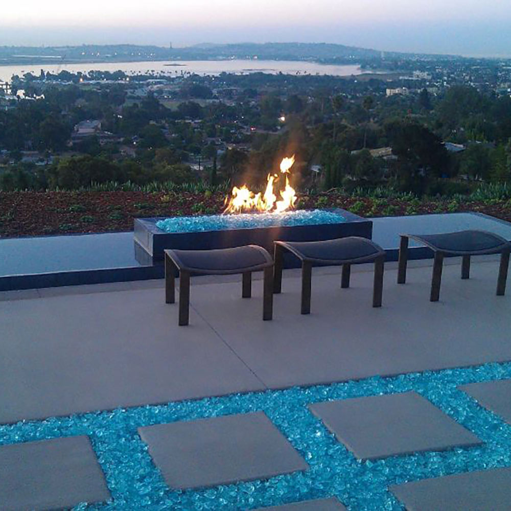 Outdoor gas fire pit with visible flame burning in a stone-lined burner area