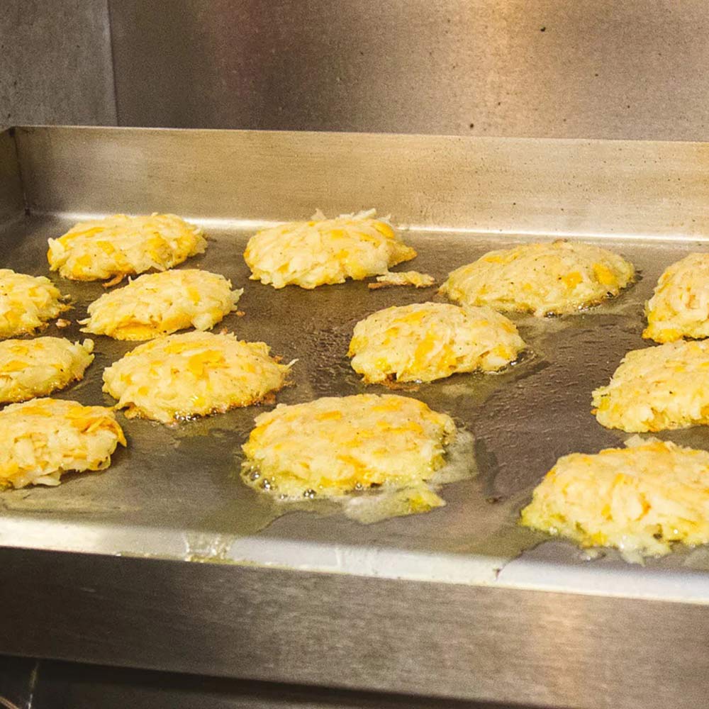 Electric griddle cooking surface with golden patties sizzling on stainless steel plate
