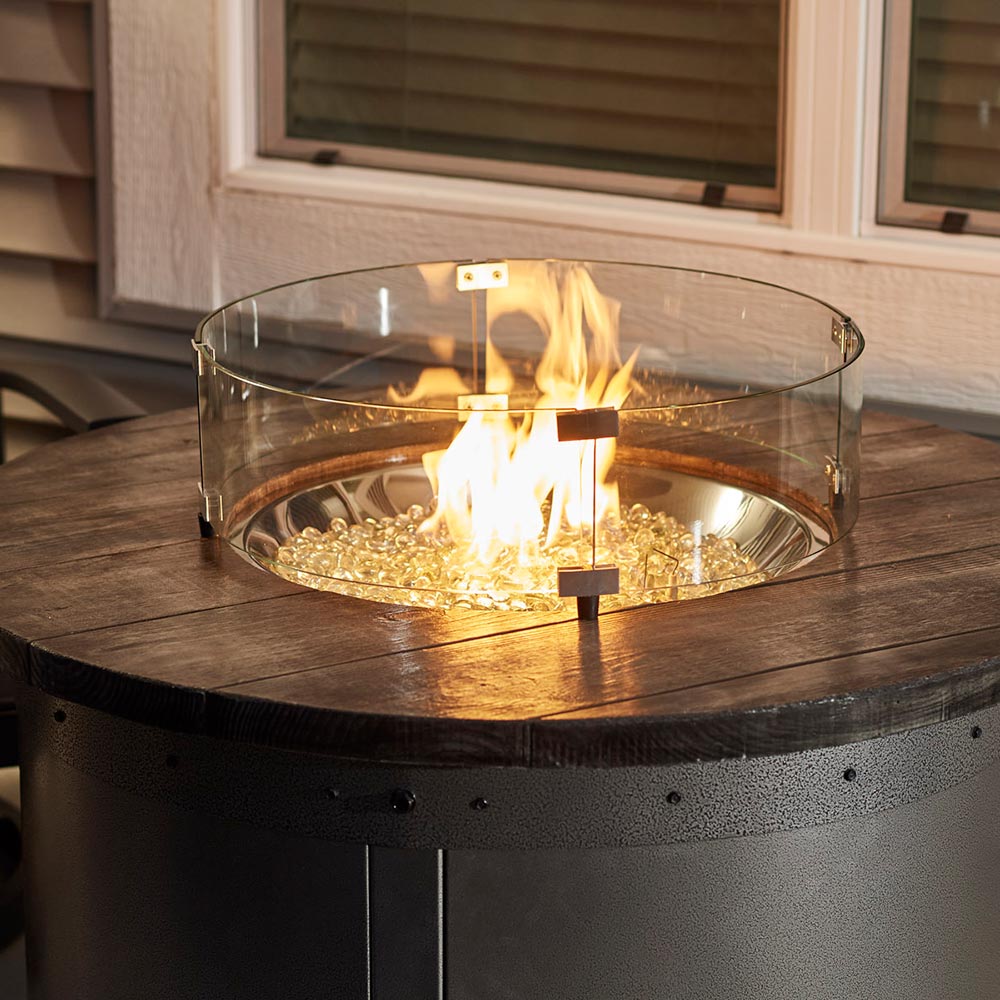 Round clear glass wind guard with flames and glowing fire bed, black base below