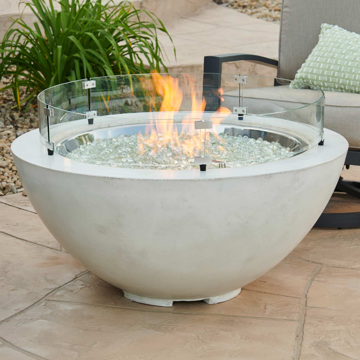 Round glass wind guard on outdoor fire bowl with flame and black mounting feet
