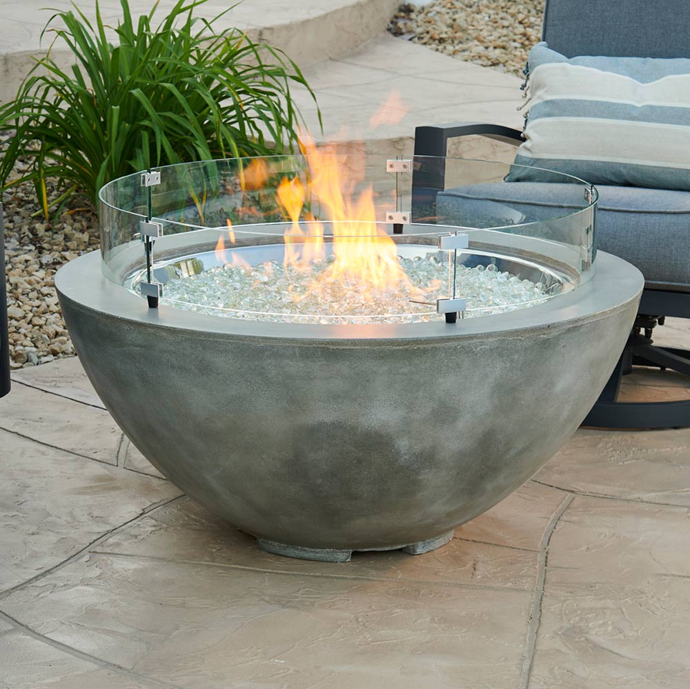 Round clear glass fire pit guard on gray bowl base with flames, metal corner clamps