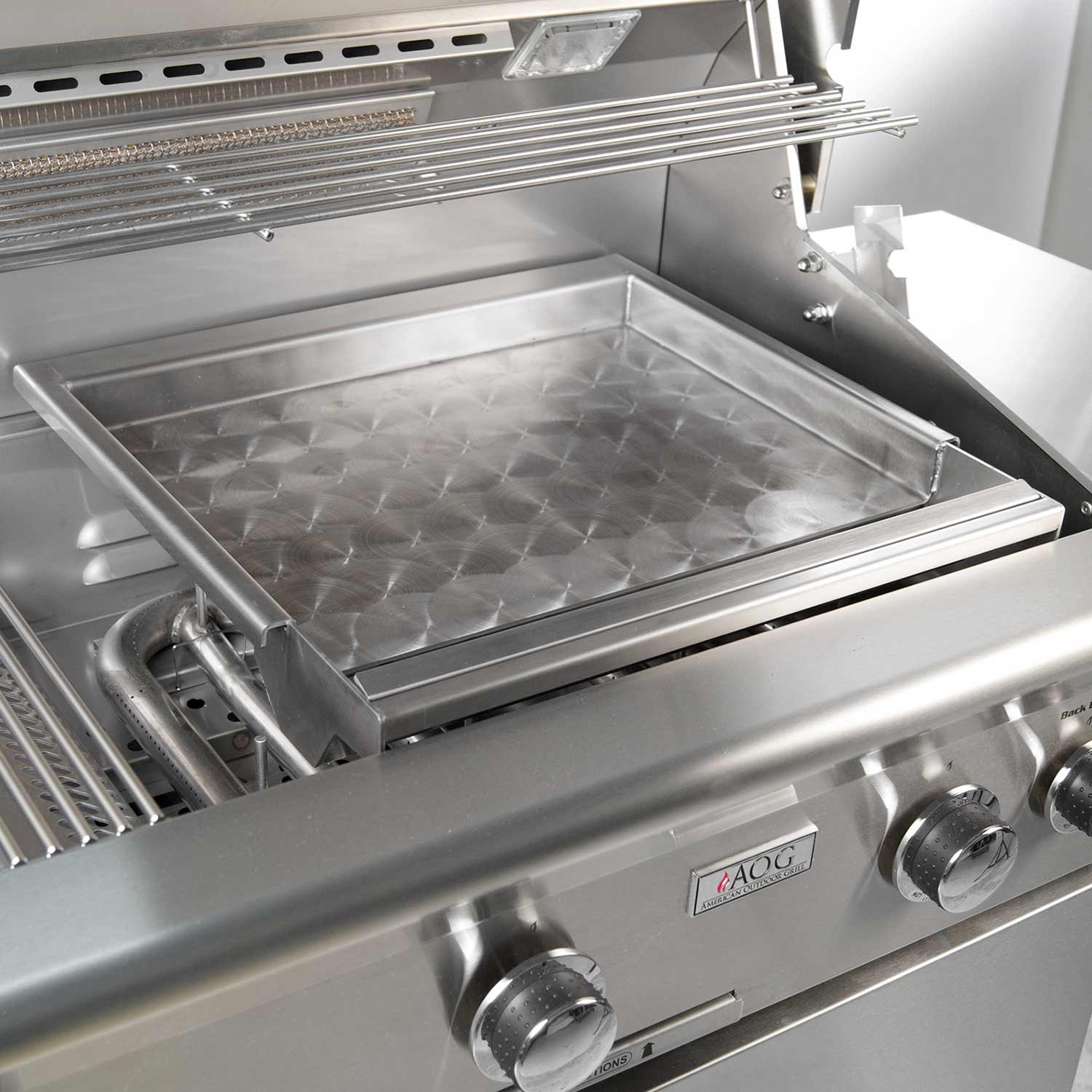 Outdoor stainless griddle tray with diamond pattern, set on a gas grill, front knobs