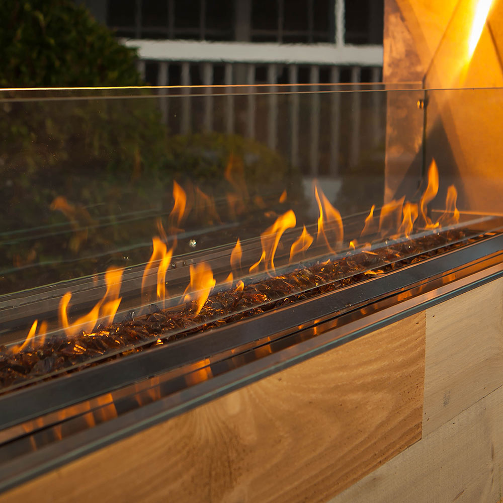 Dark reflective fireglass lining inside a linear fire pit with flames