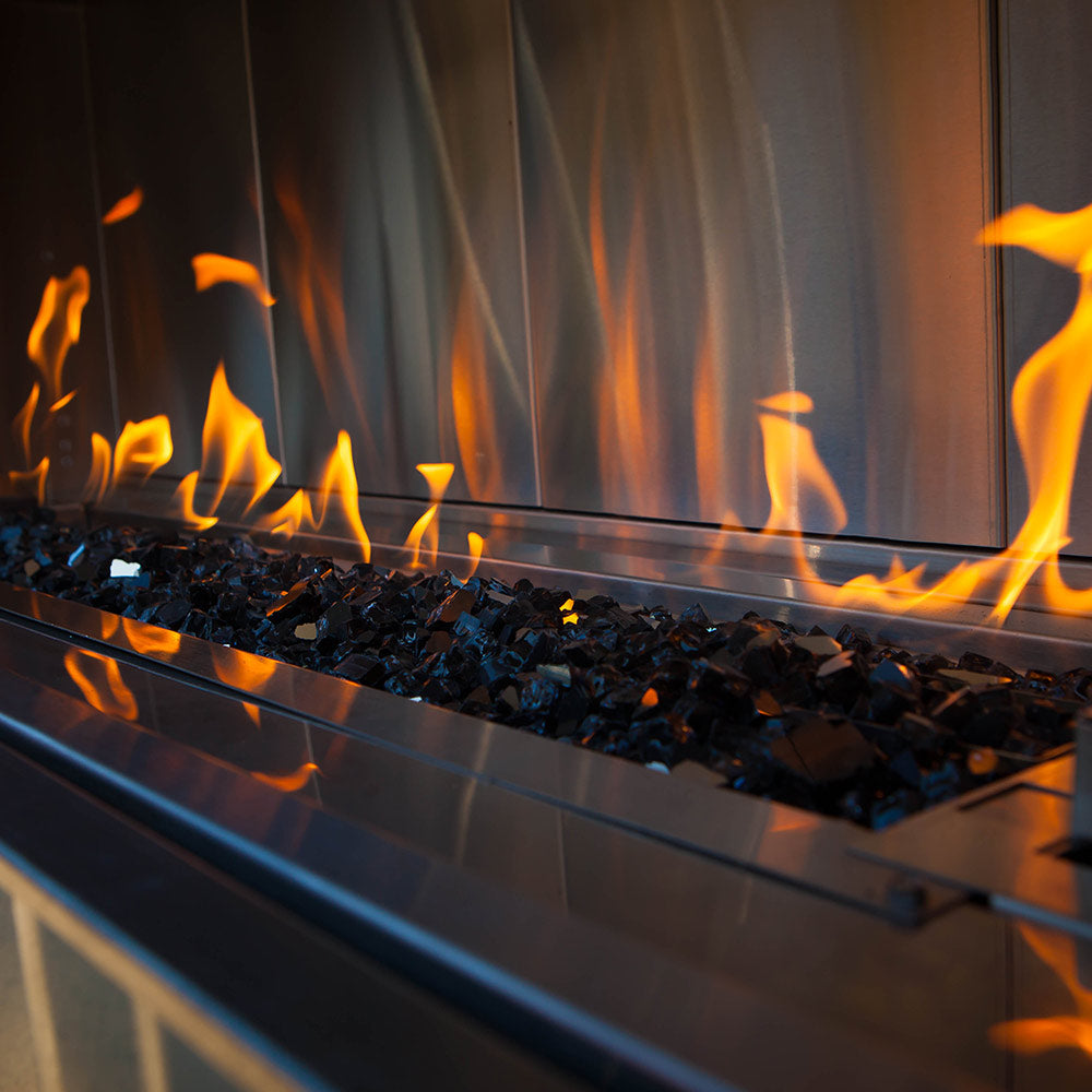 Reflective blue and dark fireglass with flames inside a linear gas fire pit