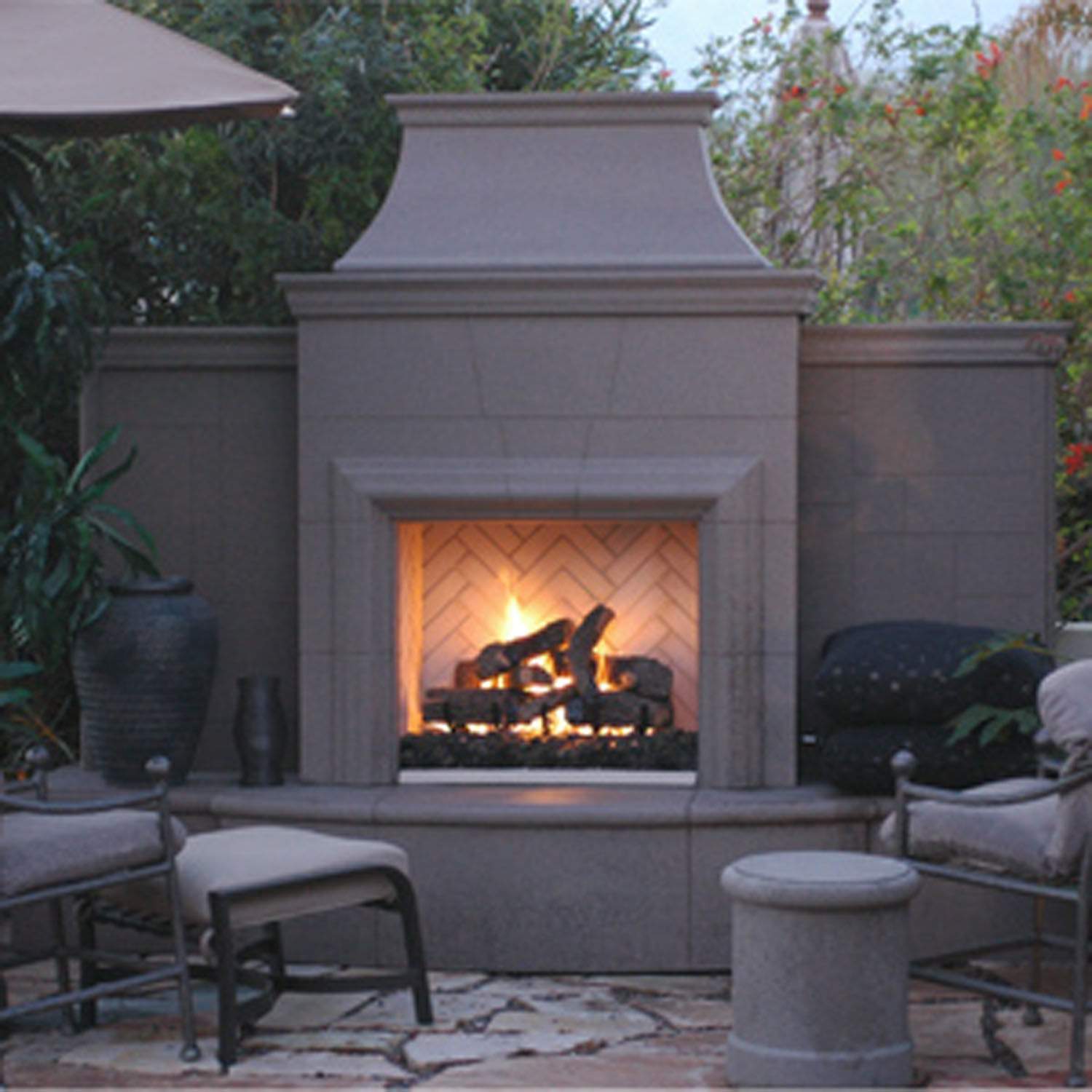 Outdoor gas fireplace with gray stone facade and open glass firebox glowing with flames