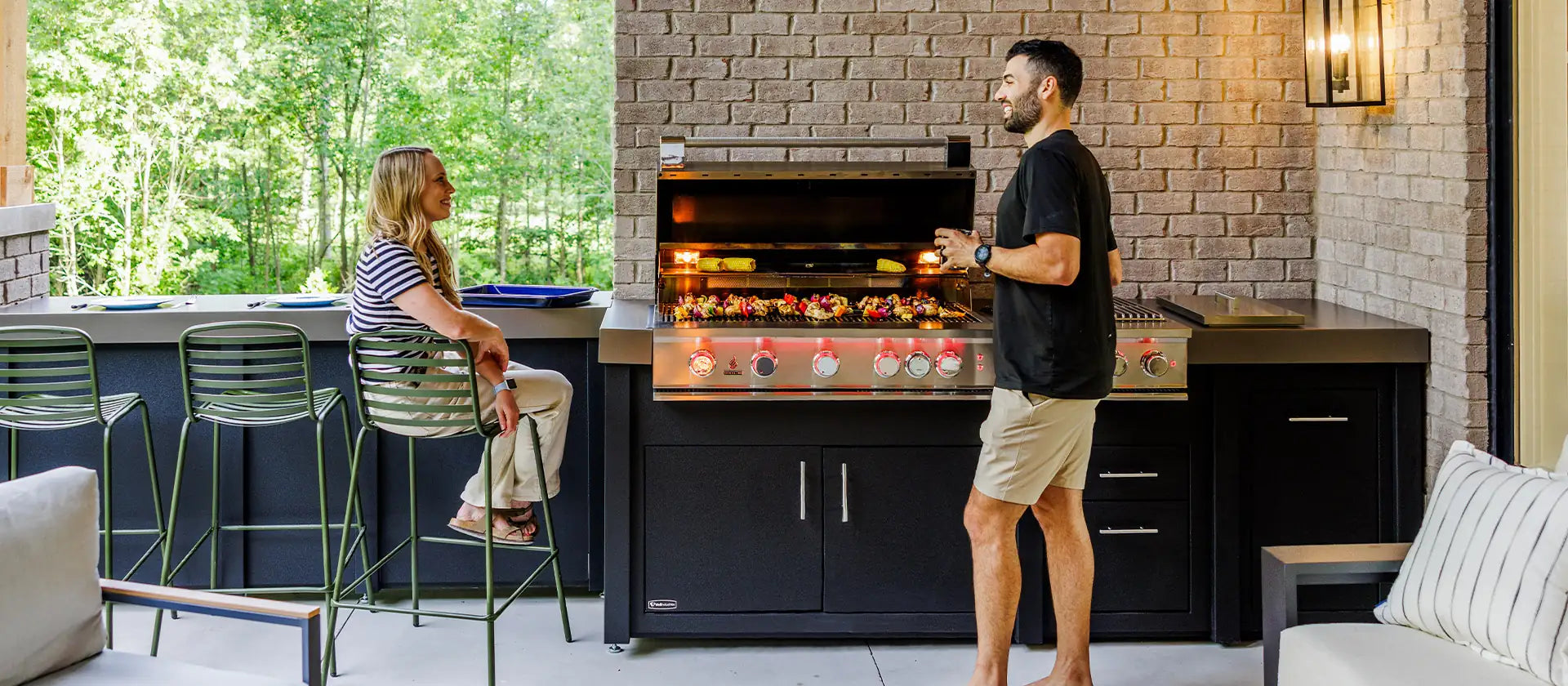 Couple cooking on a built-in outdoor kitchen grill in a covered patio