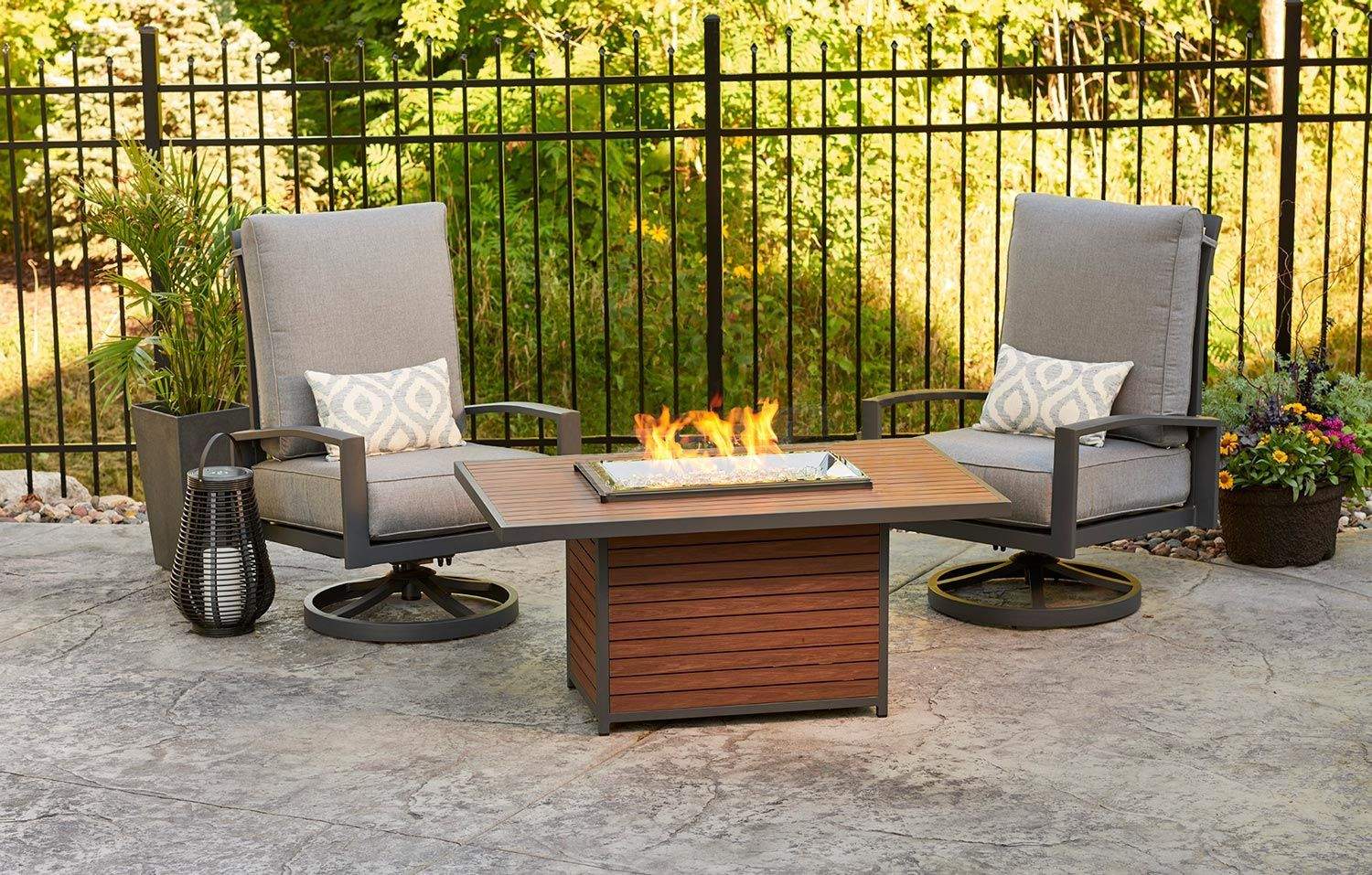 Outdoor gas fire pit table with flames, flanked by patio lounge chairs and side trays