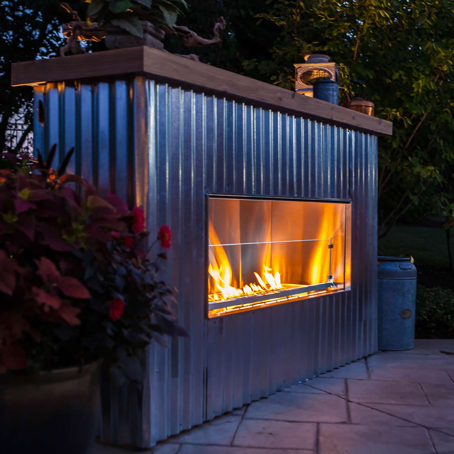 Outdoor linear fireplace with lit burner and flame visible through front glass