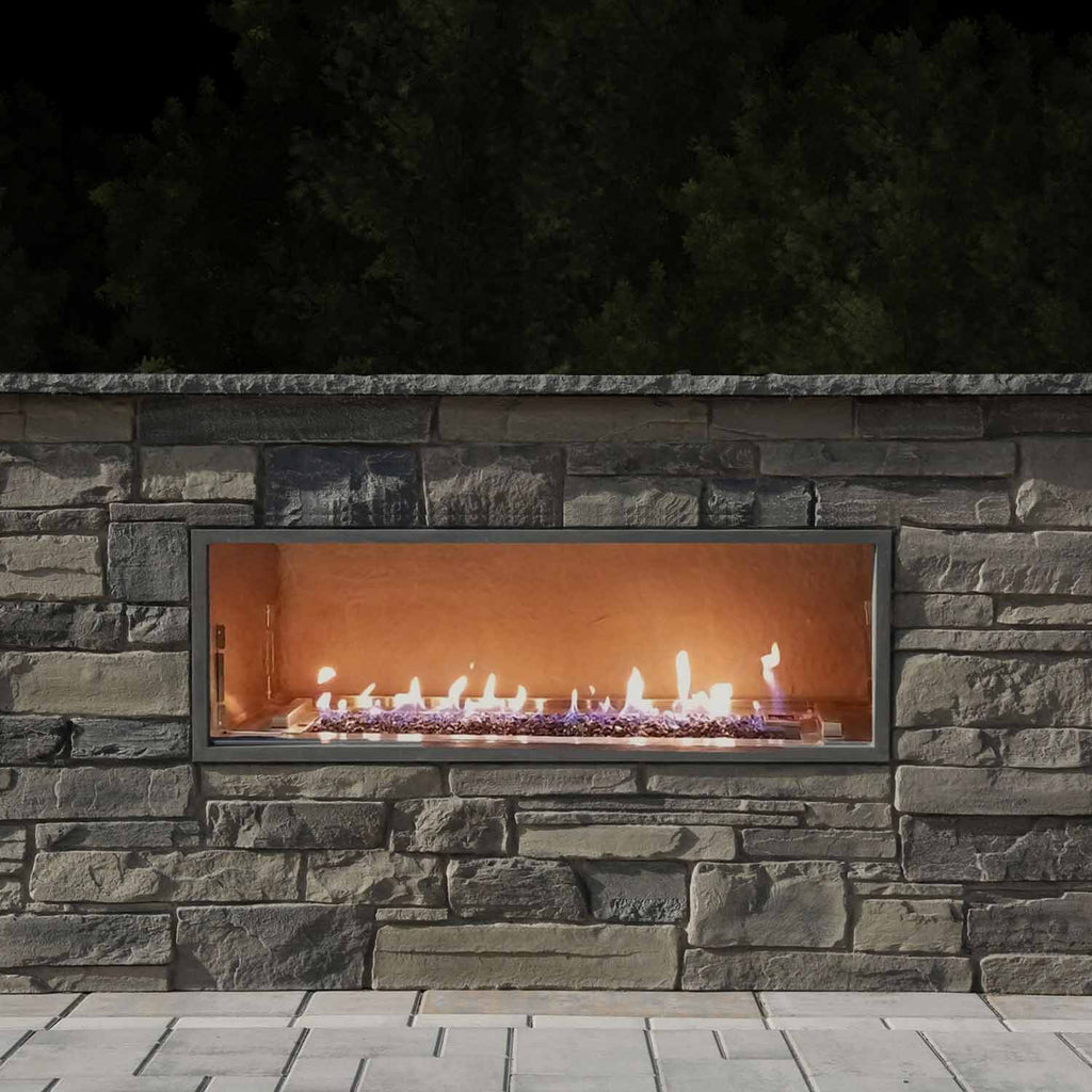 Linear outdoor gas fireplace insert set in a gray stone wall