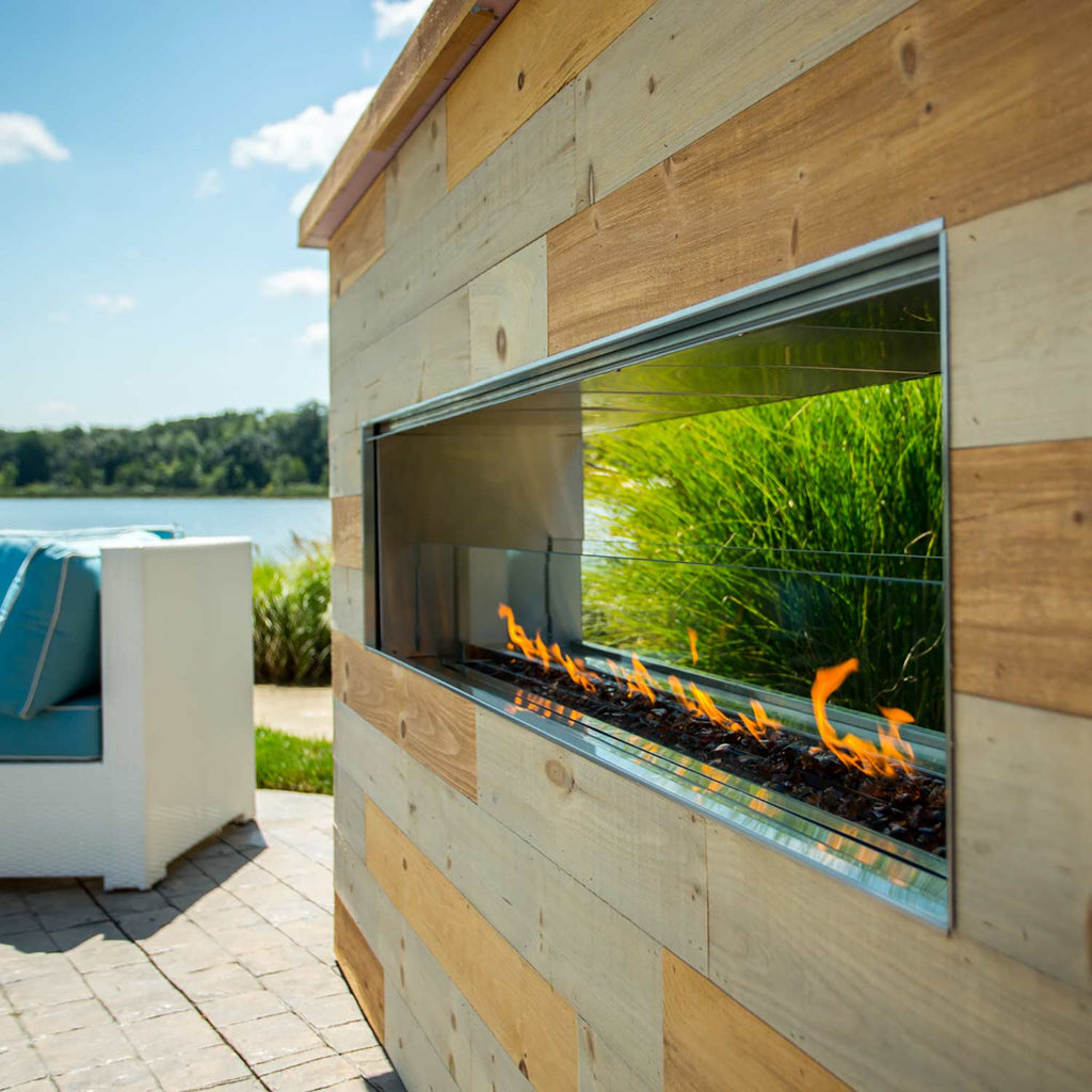 Outdoor linear see-through gas fireplace installed in a wood wall with flames and glass front.