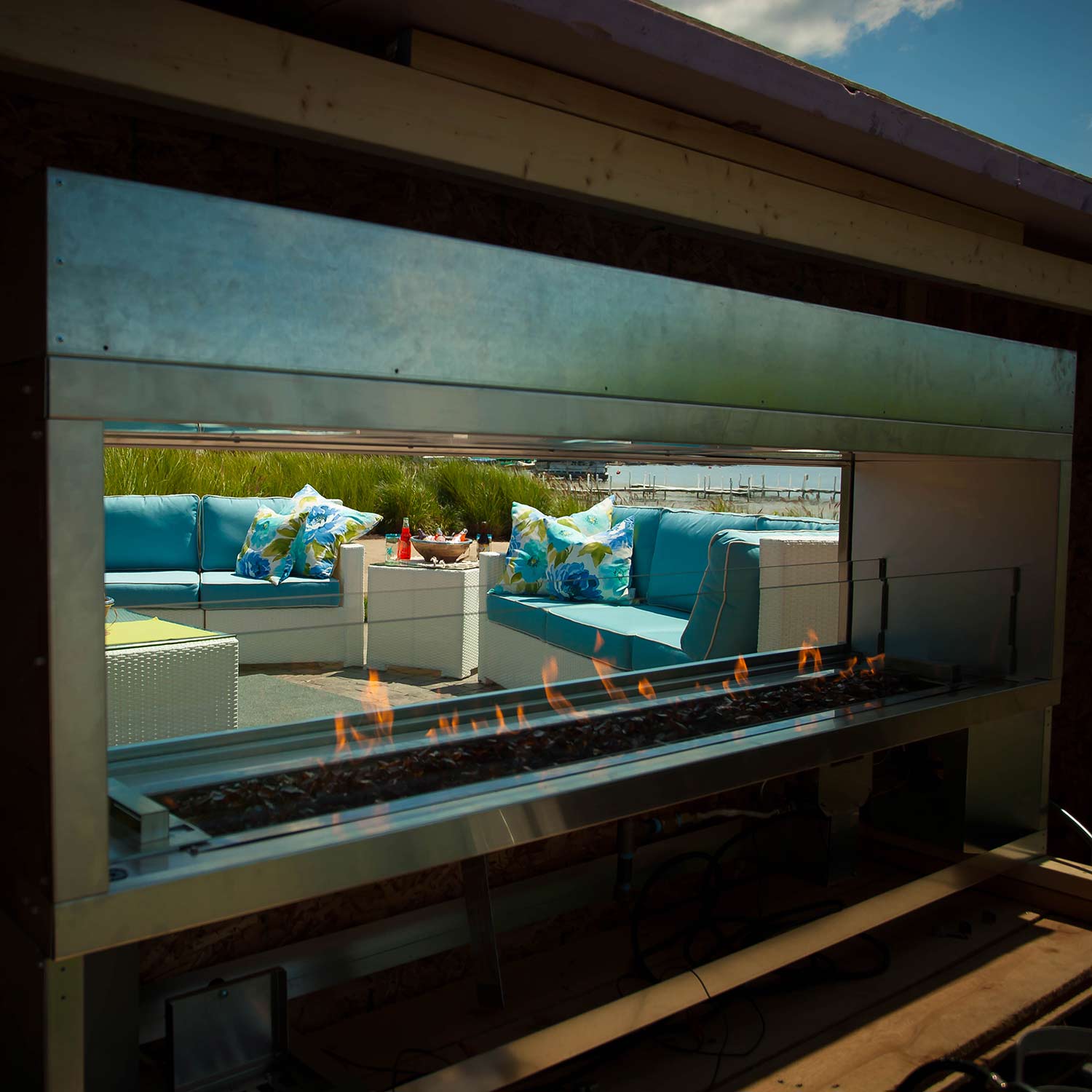 Outdoor linear glass gas fireplace with flames glowing through clear panel, stainless frame.
