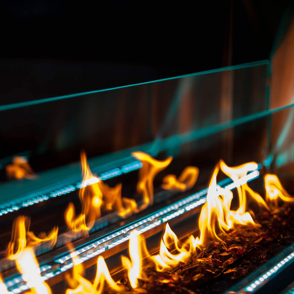 Close-up of linear see-through outdoor gas fireplace flames behind glass and LED strips