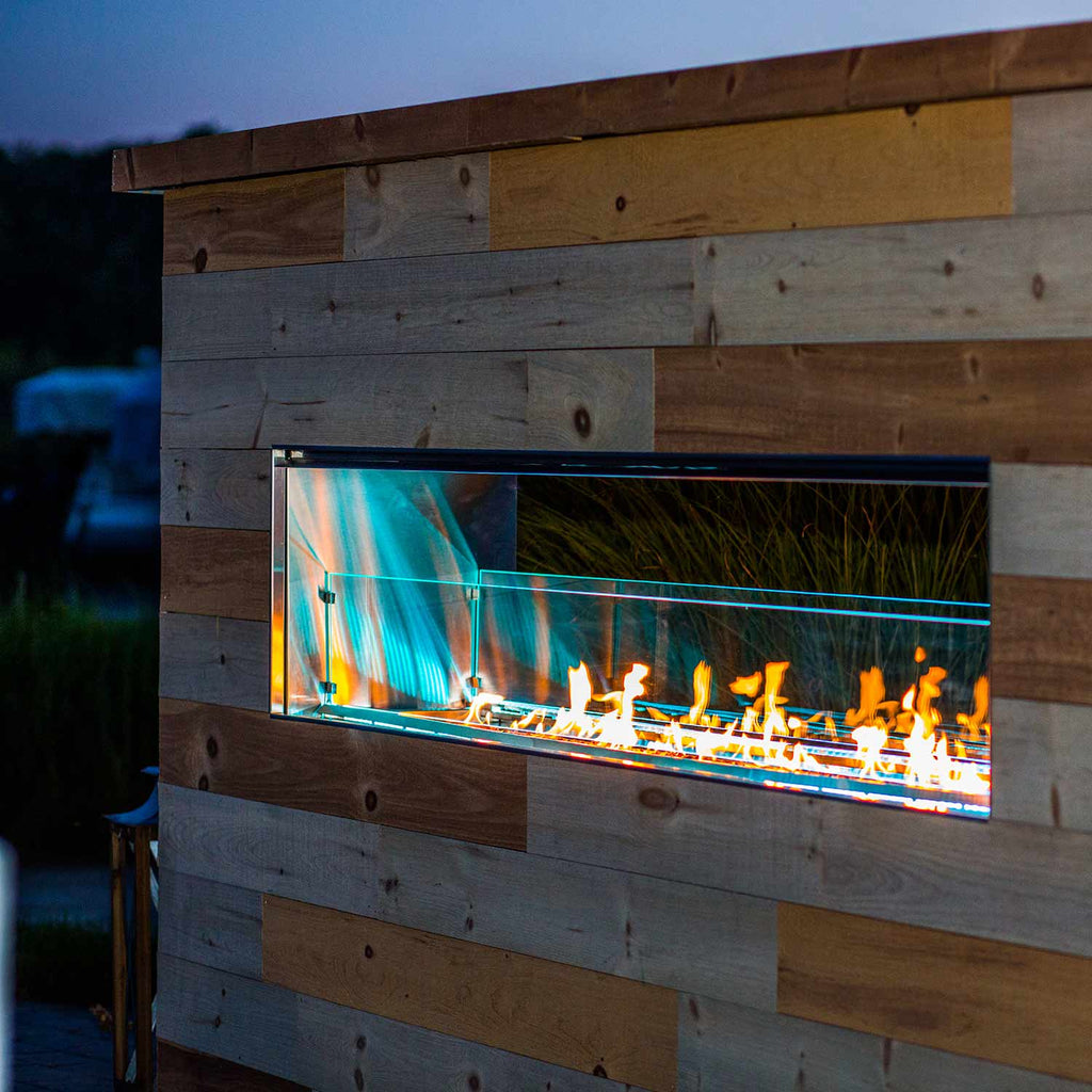 Outdoor linear see-through gas fireplace with blue LED glow and orange flames behind glass