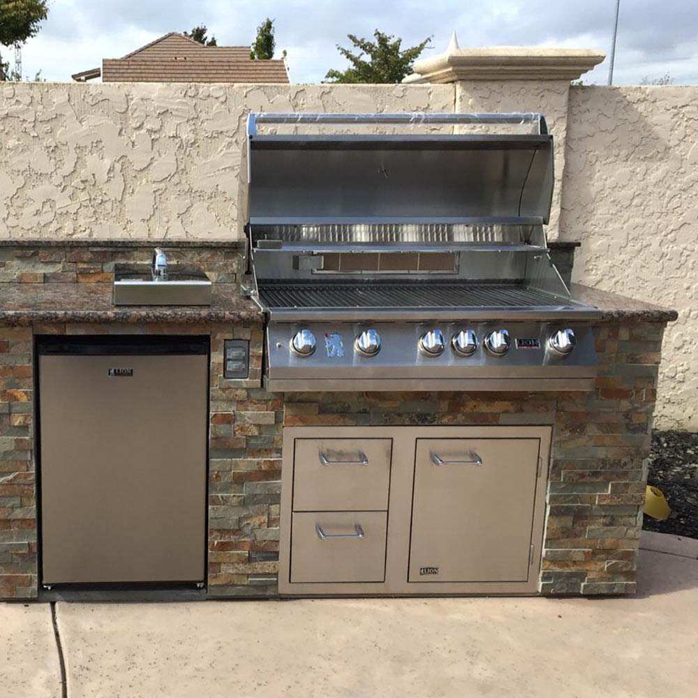 Built-in stainless steel grill installed in outdoor kitchen with open lid and control knobs