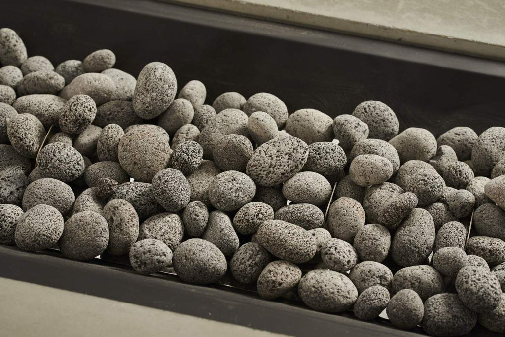 Tumbled lava rock, dark gray pebbles with porous, textured surface in a tray