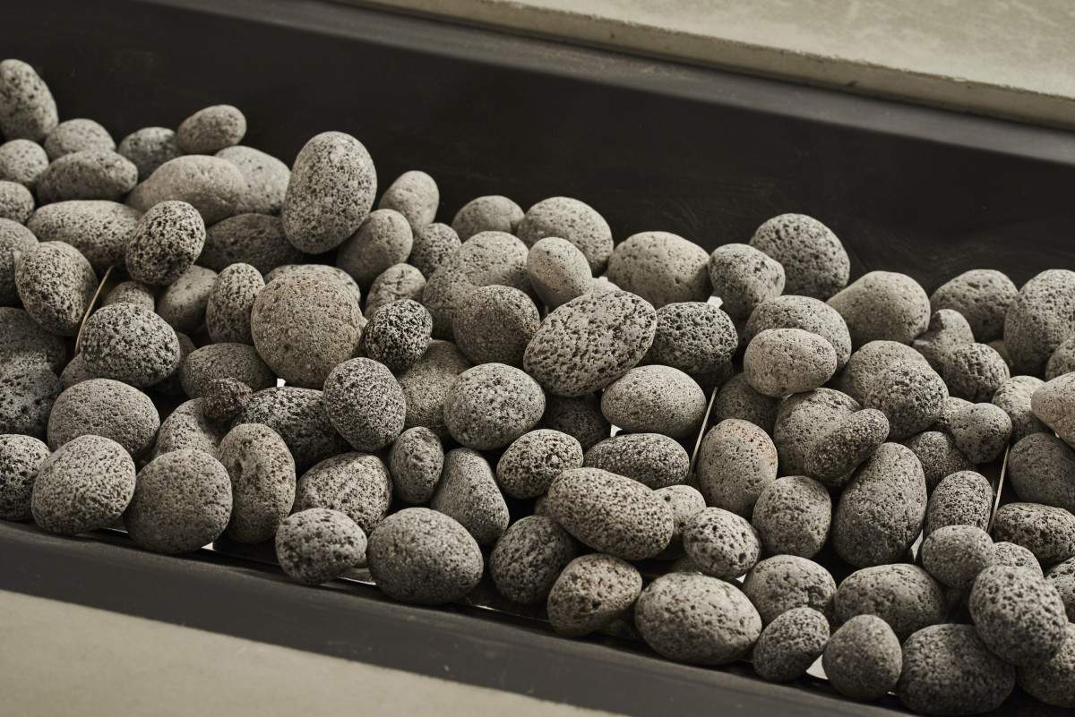 Tumbled lava rock, dark gray pebbles with porous, textured surface in a tray