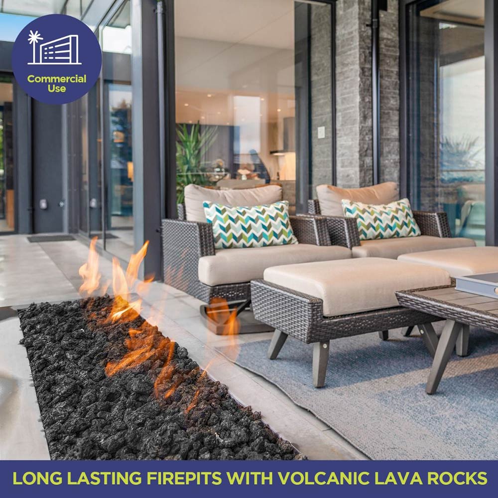 Black lava rocks lining a firepit with flames outdoors near patio seating