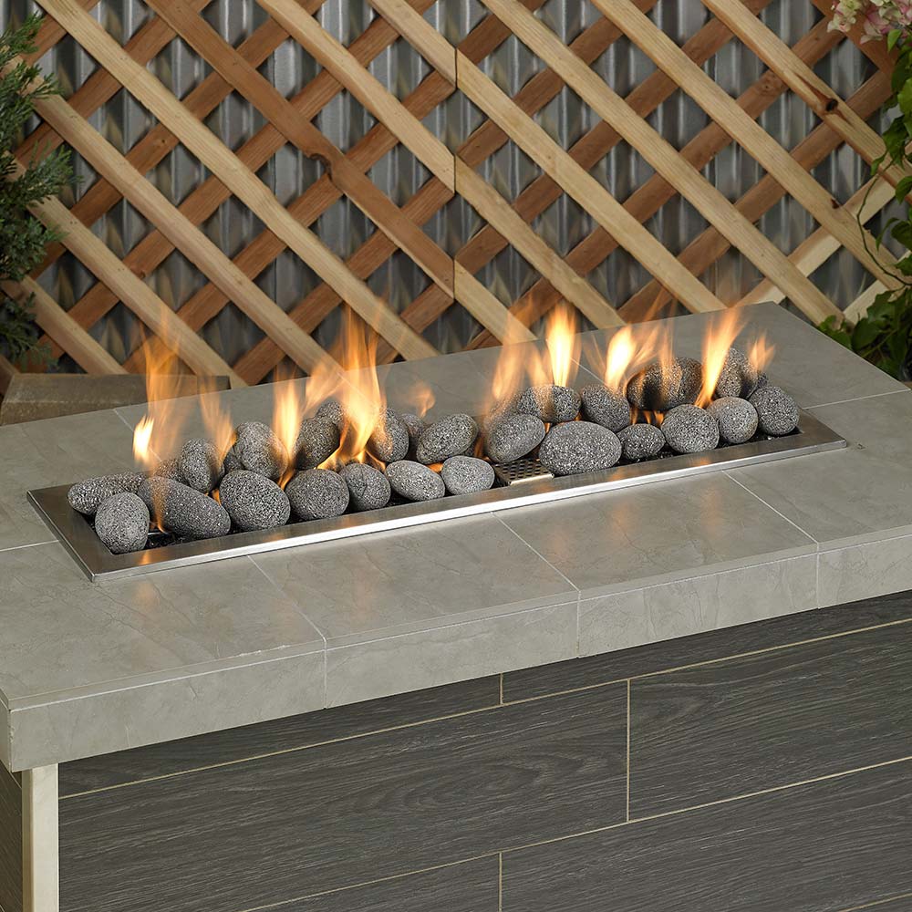 Gray lava stones filling a linear fire pit tray, smooth rounded rocks