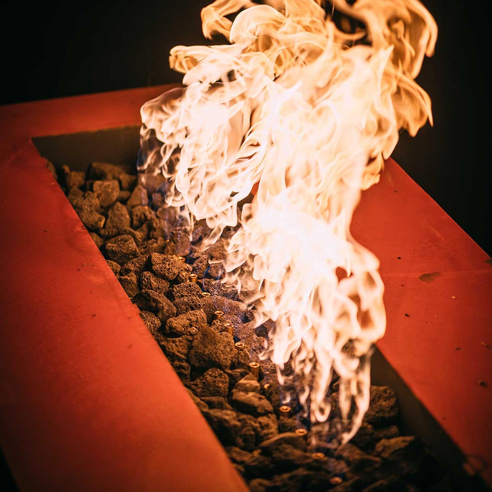 Linear gas fire pit burner with glowing rocks and tall orange flames