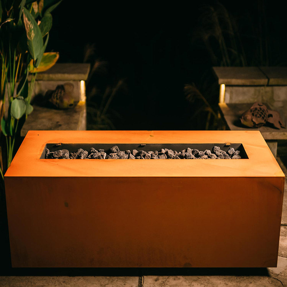 Rectangular bronze gas fire pit with open burner and dark lava rocks