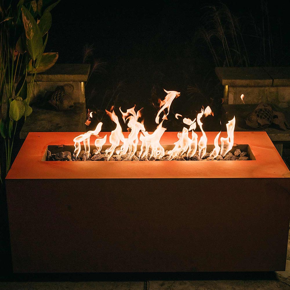 Copper-tone linear gas fire pit with flames burning across the burner tray