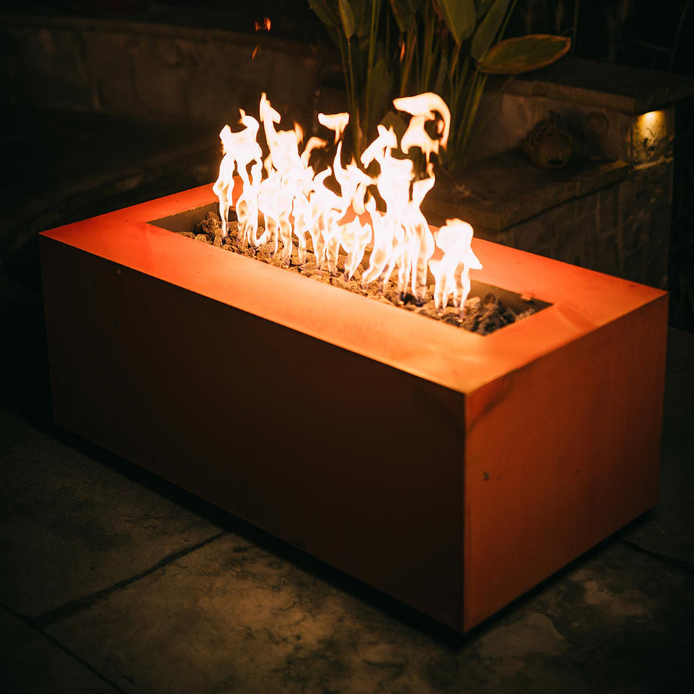 Corner view of copper-tone linear gas fire pit with flames over burner tray