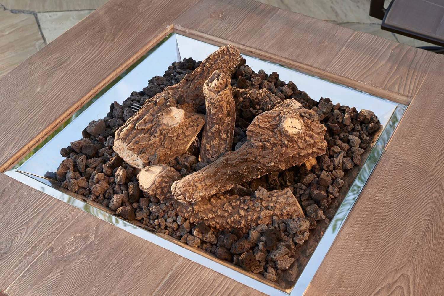 Outdoor gas fireplace log set with brown logs and black lava rock in burner tray