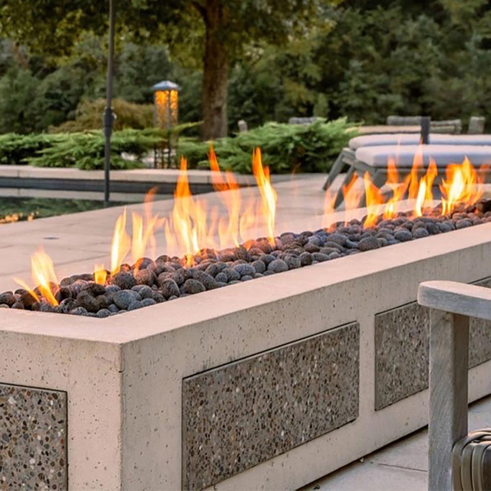 Outdoor rectangular gas fire pit with glowing flames over dark lava rocks