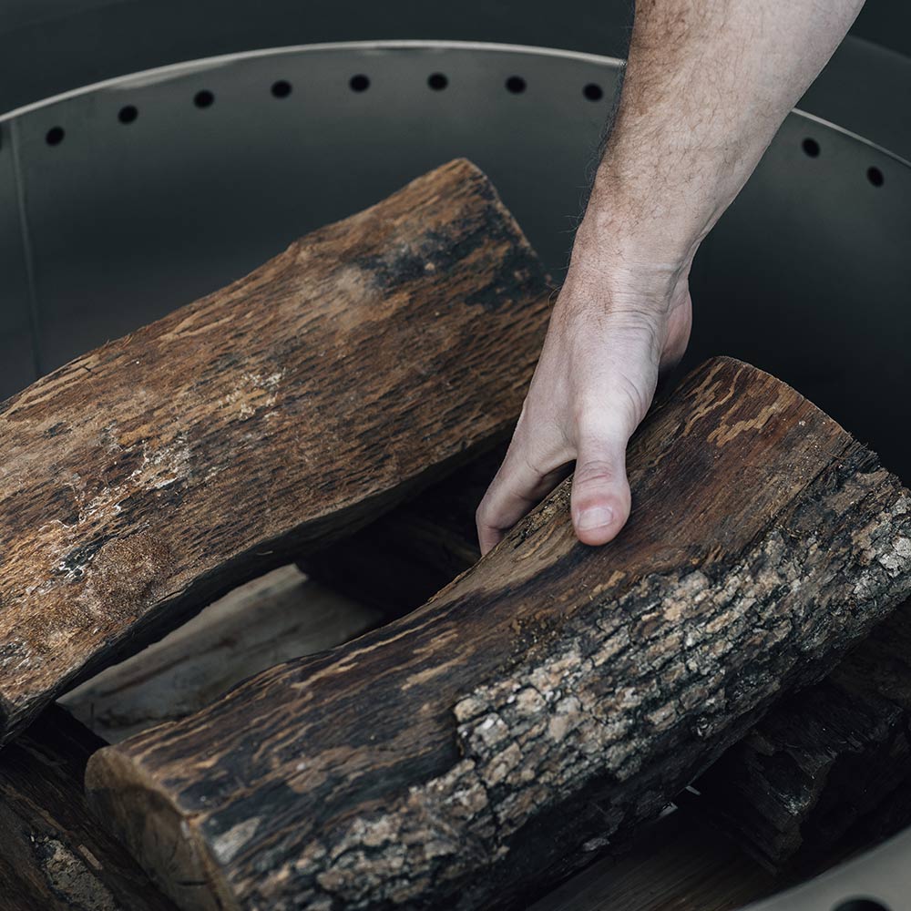 Hand placing logs into a round fire pit with perforated top ring