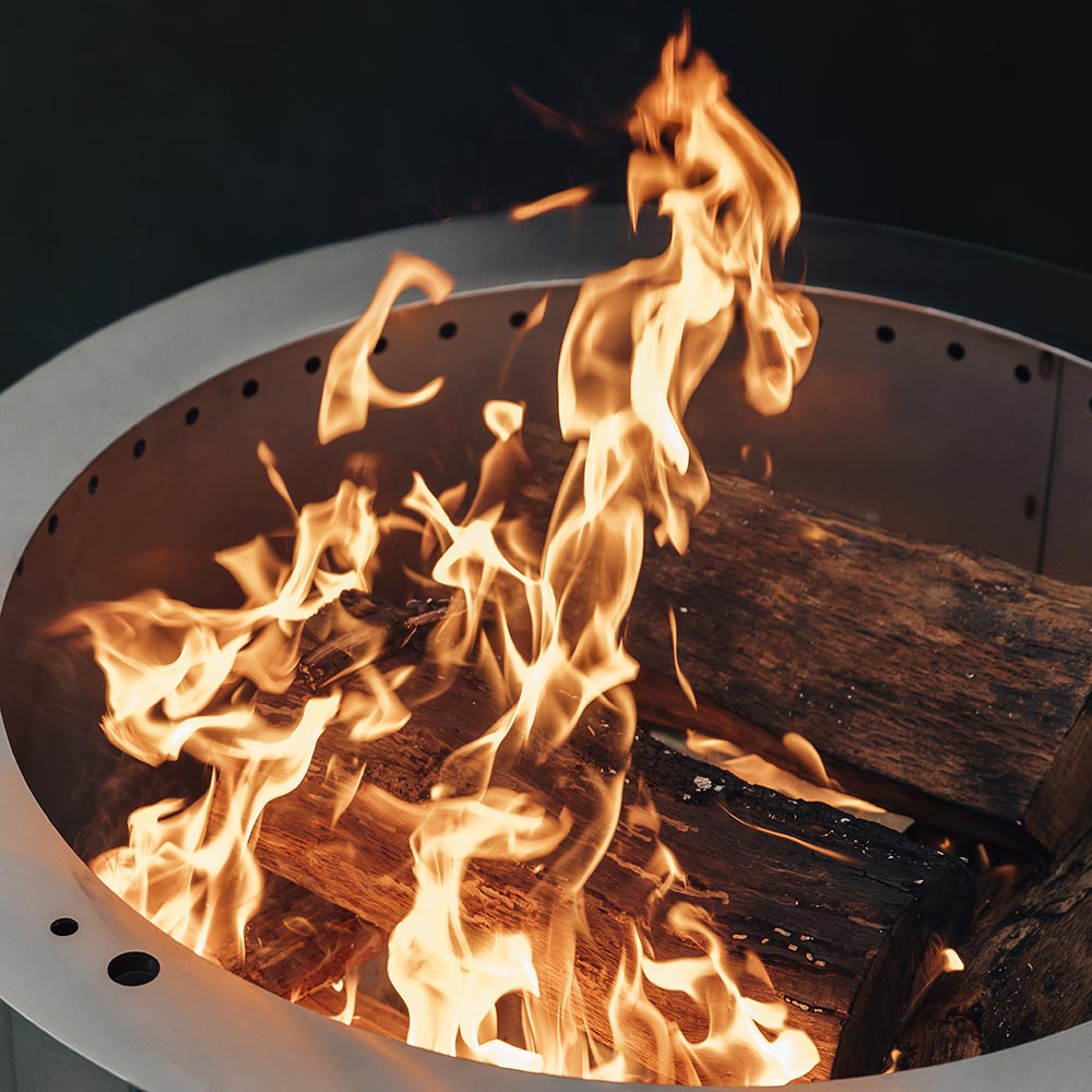 Open fire pit with visible flames over logs on the perforated cooking surface