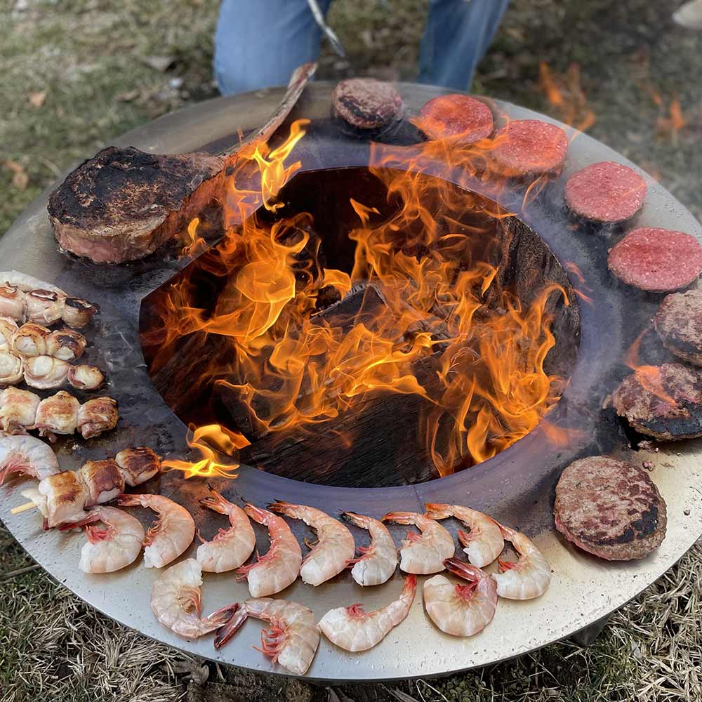 Fire pit cooking surface with shrimp and burgers, flames rising from the grill bowl