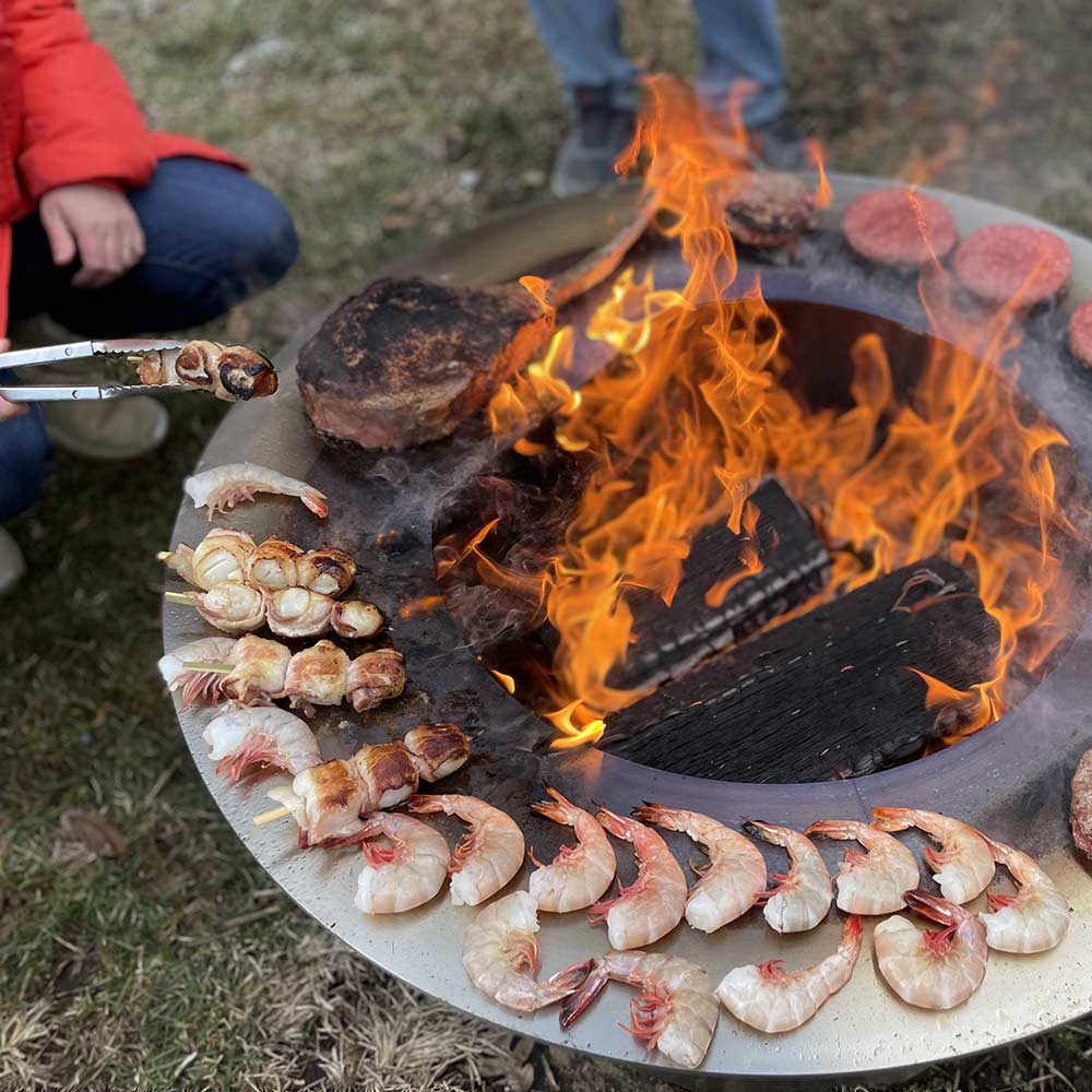 Smokeless fire pit cooking surface with shrimp and steaks over open flames