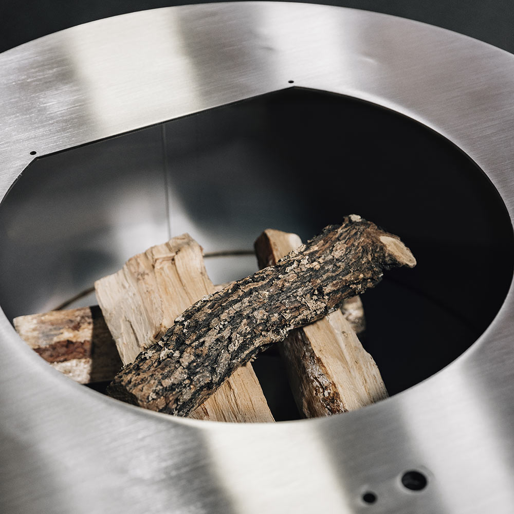 Steel fire pit bowl with stacked wood logs at the center and a vent hole