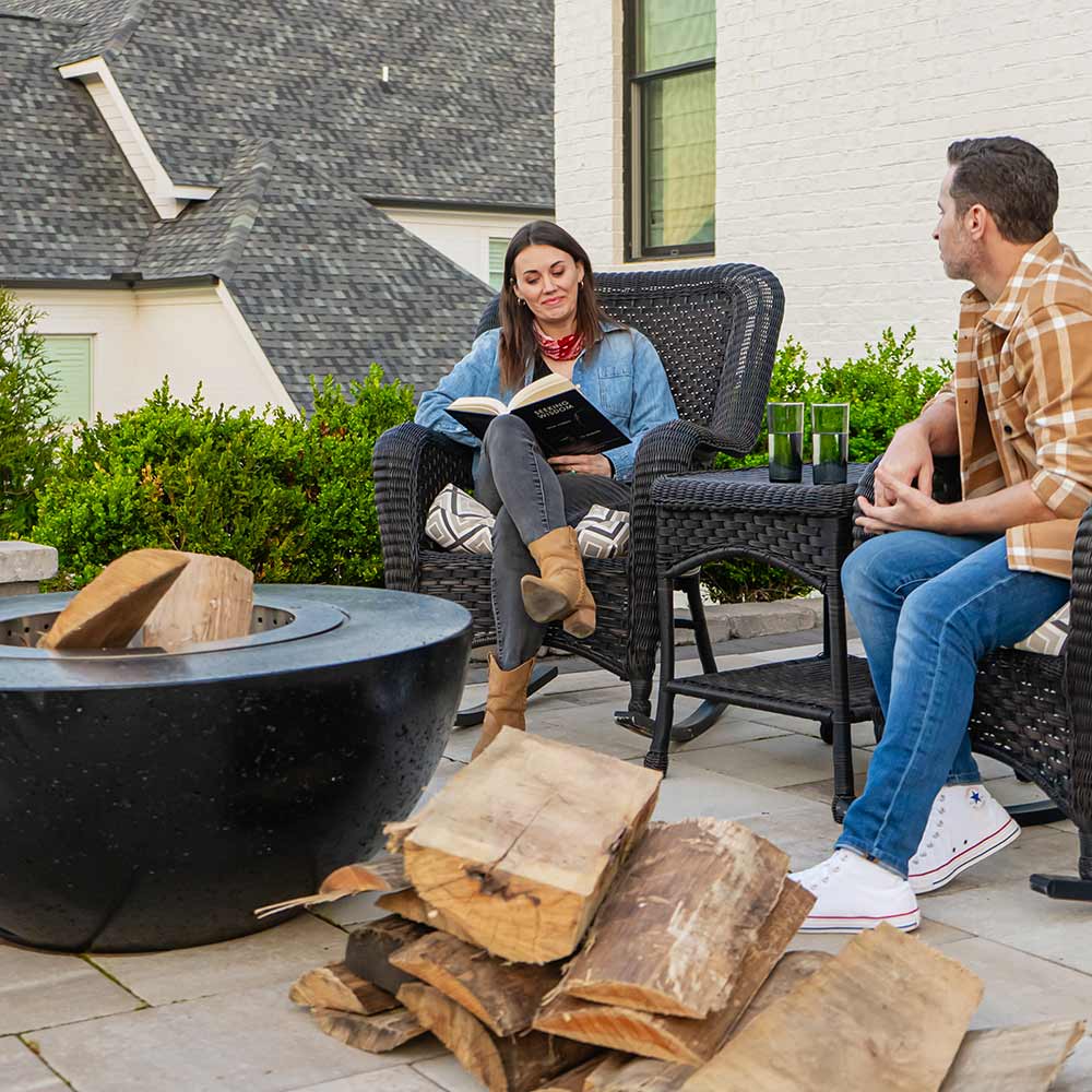 Dark GFRC wood fire bowl with smokeless stainless steel insert beside stacked logs