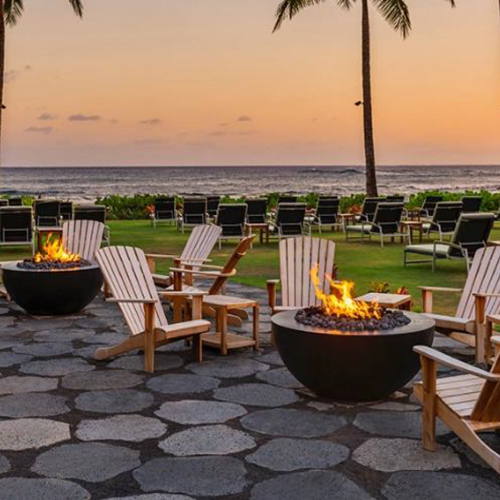 Outdoor fire pit table with dark bowl and visible flame, with patio chairs around