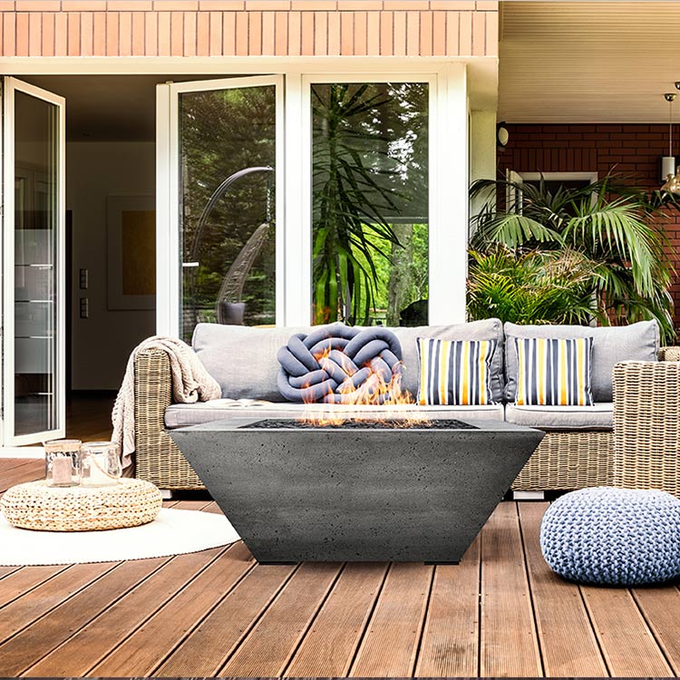 Concrete gas fire pit with flames in a rectangular fire bowl on an outdoor deck