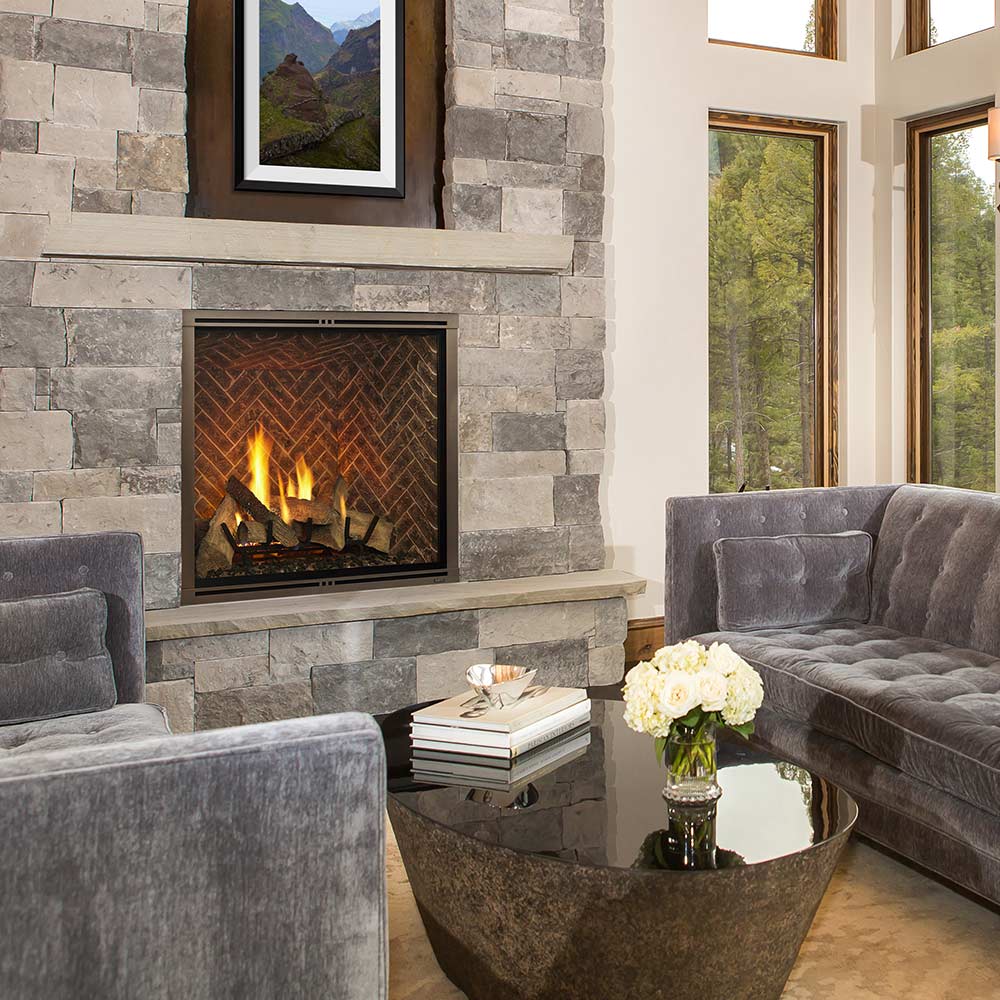 Living room with stone fireplace, gray sofa, and coffee table with flowers.