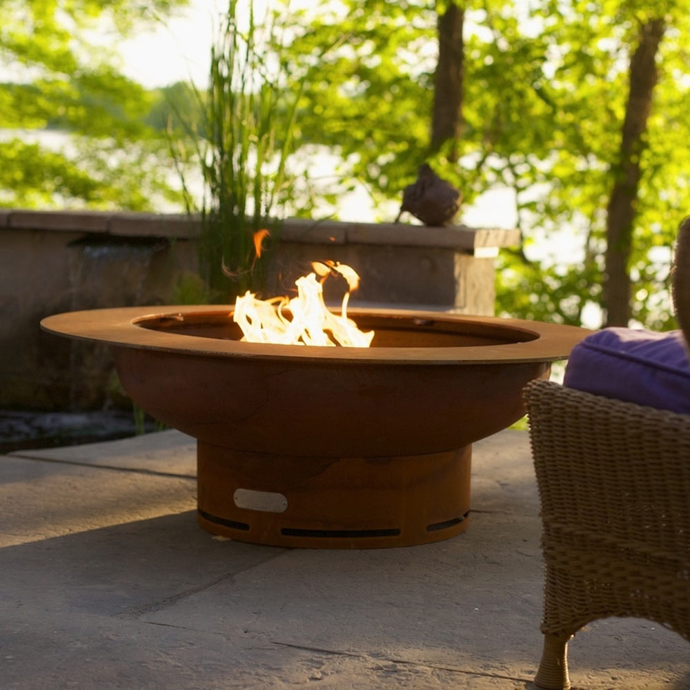 Copper-toned gas fire pit with flames in a round fire bowl on patio